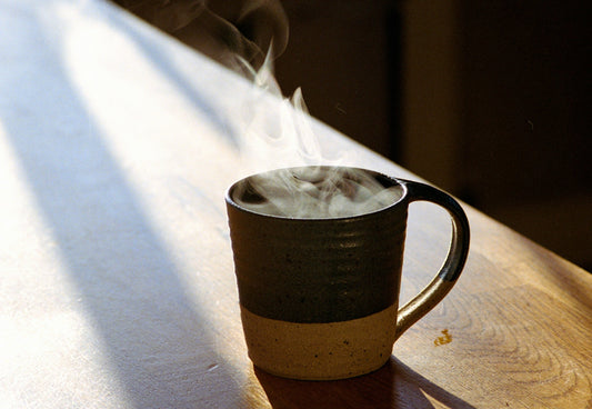 Steam rises from a stoneware mug catching low light on a wooden table